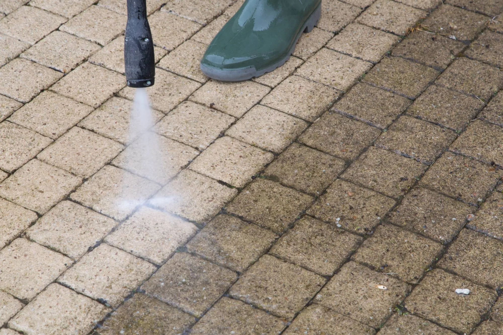 A pressure washer cleaning a paver walkway, with clean pavers beside dirty ones